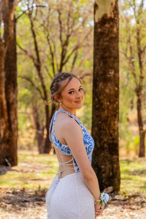 An elegant white and blue patterned dress with cutout details is showcased in a forest setting.