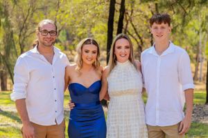 Group photo outdoors with four people dressed in formal attire against trees.