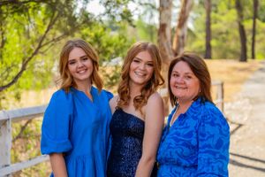 Three people in blue and navy dresses pose together on outdoor path.