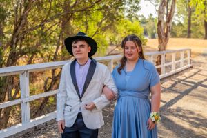 Couple in formal wear walking together on wooden bridge pathway.