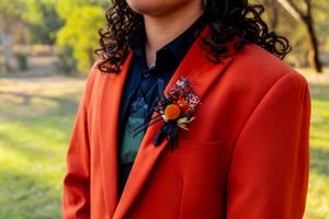 A detailed view of an orange suit jacket with floral boutonniere against a sunny outdoor background.