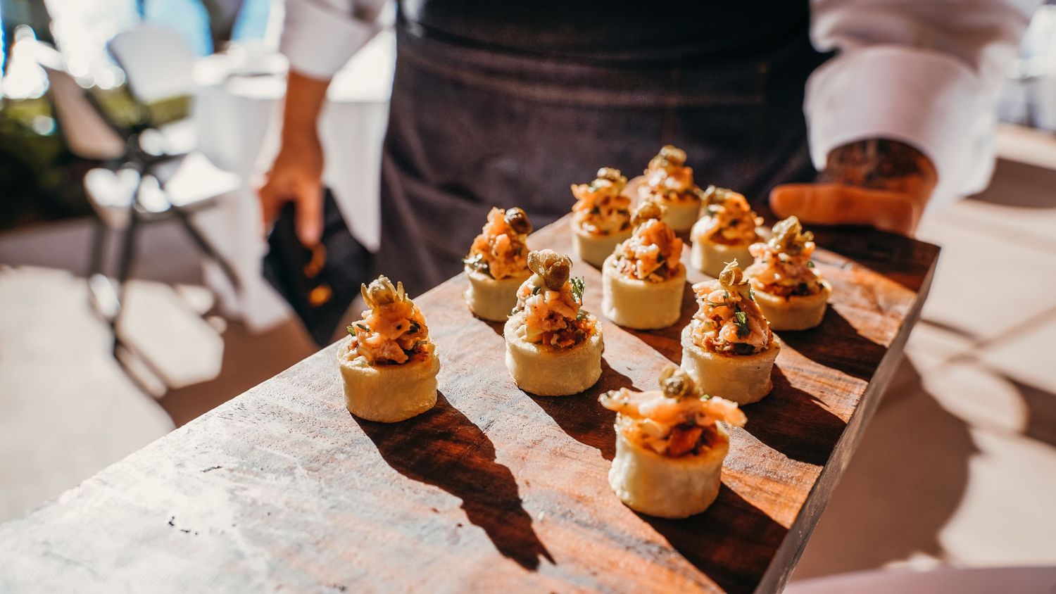 Golden appetizers arranged on a wooden serving board cast dramatic shadows in sunlight.
