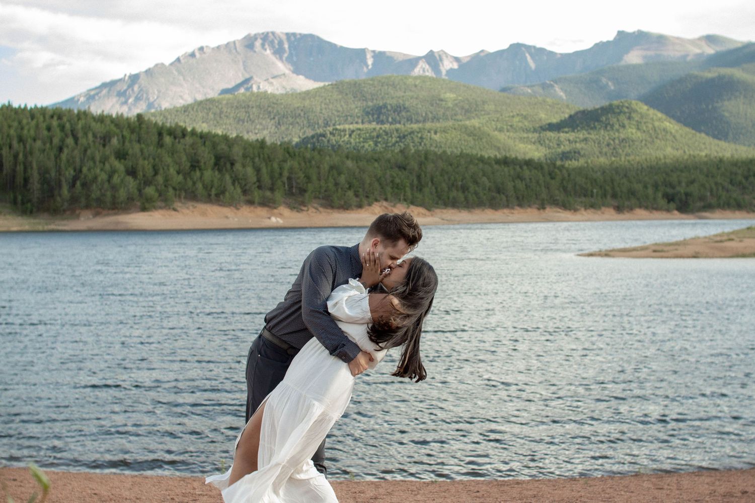 A romantic embrace by a mountain lake with snow-capped pike peaks and evergreen forests in the background. Colorado elopement photographer