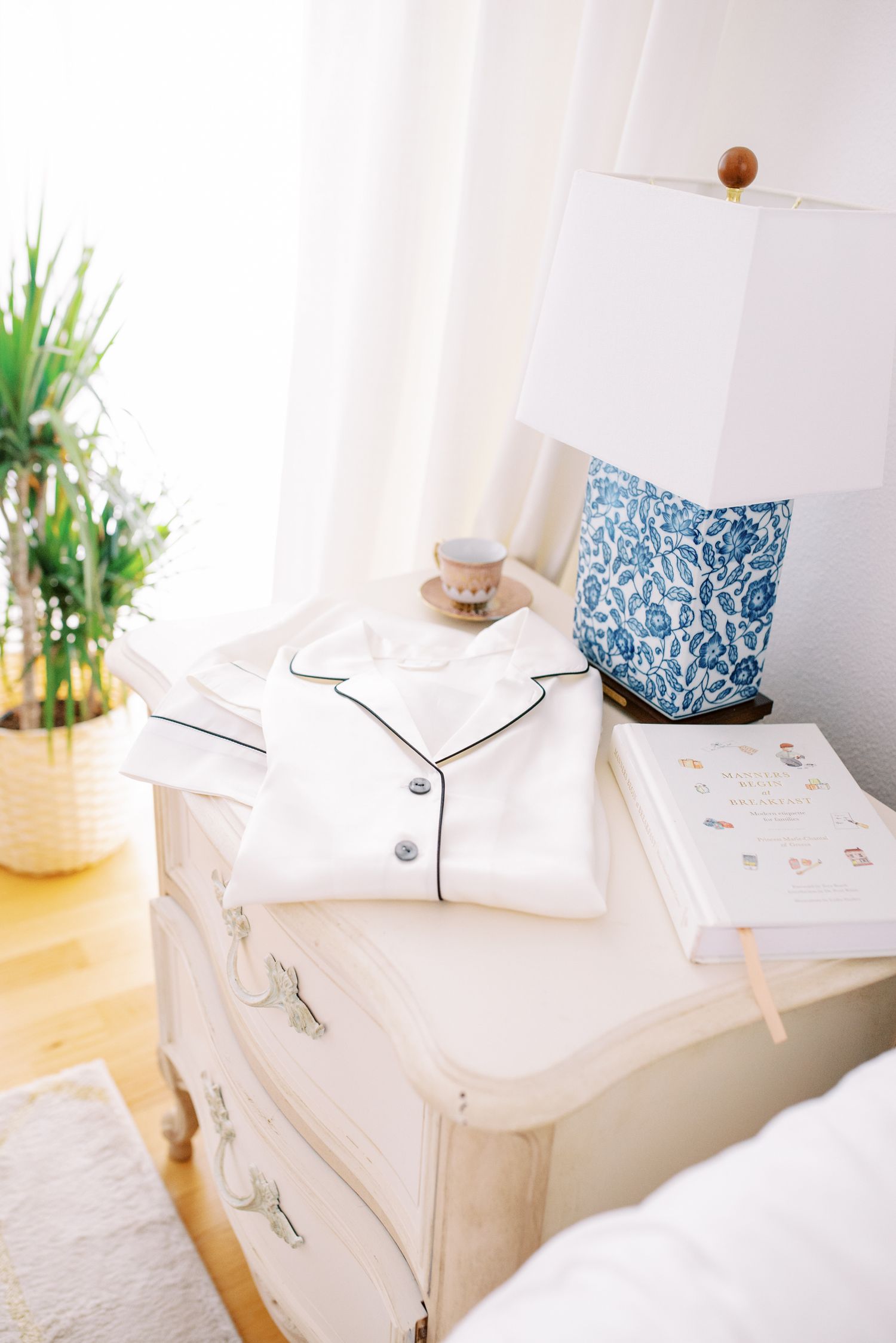 Cozy bedroom scene with white pajamas and blue patterned lamp on vintage dresser.
