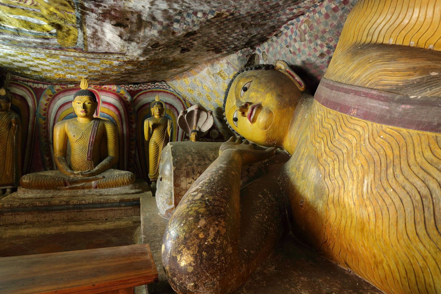 Ancient reclining Buddha statues in golden color inside cave temple.