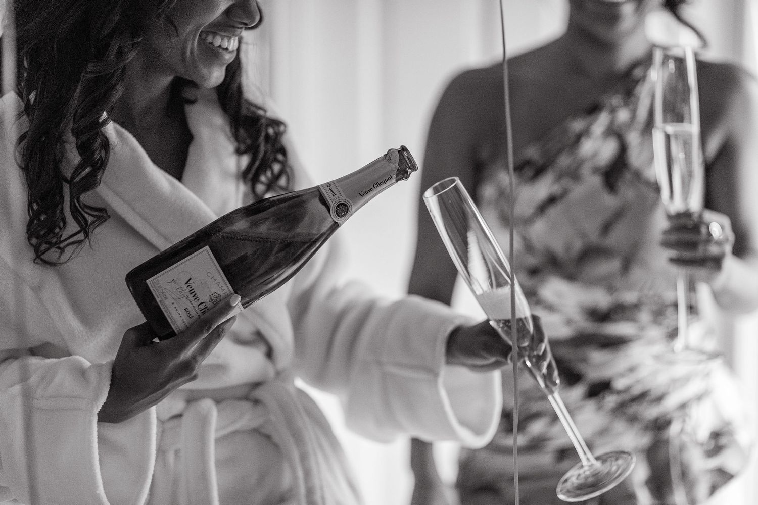 Black and white image of champagne being poured into glasses during wedding preparation.