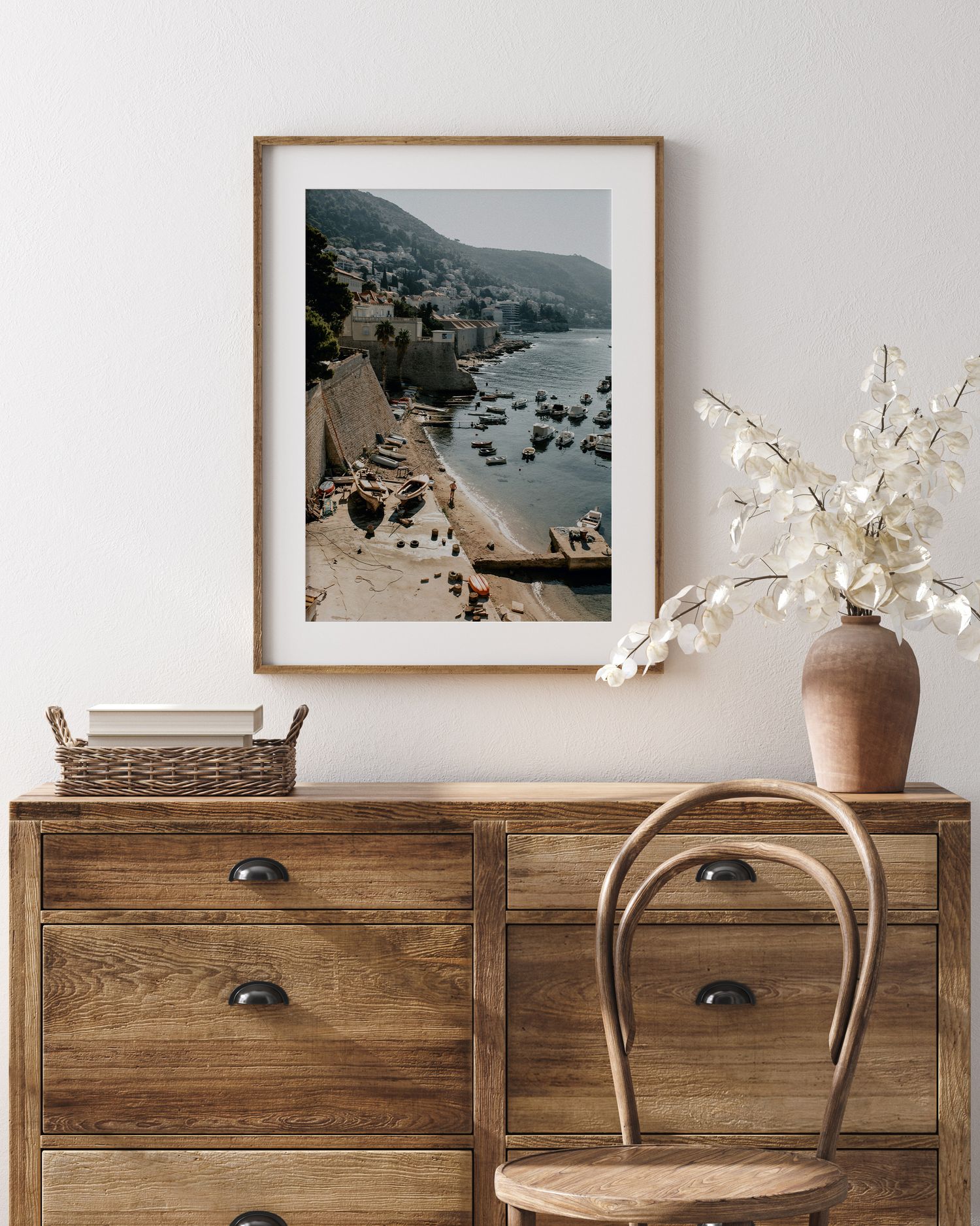 Coastal landscape photograph in wooden frame showing boats and rocky cliffs displayed on vintage dresser.