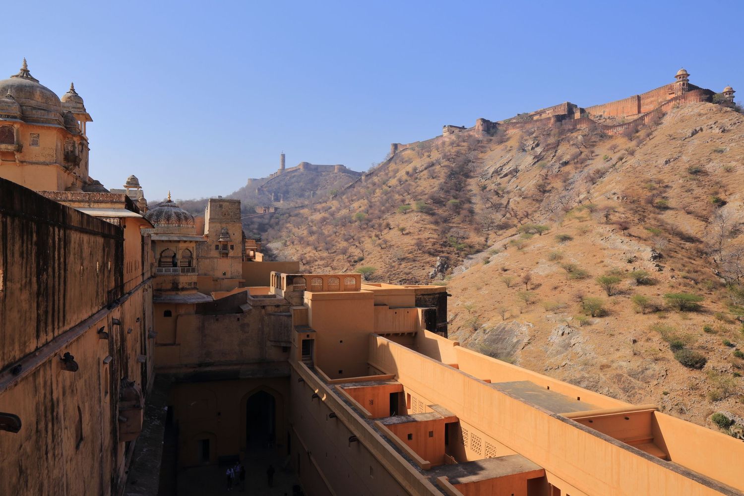 Historic architecture of Amber Fort with mountain fortifications visible in background under blue sky.