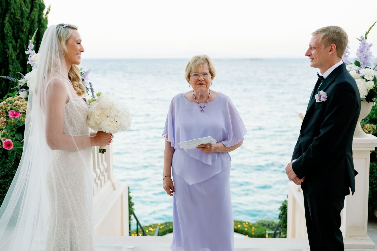 Seaside wedding ceremony with white floral arrangements and Mediterranean backdrop.