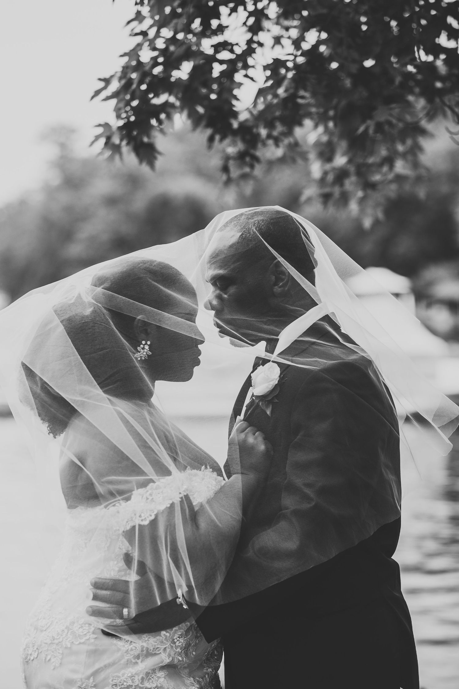 Black and white photo of bride and groom sharing intimate moment under flowing wedding veil.