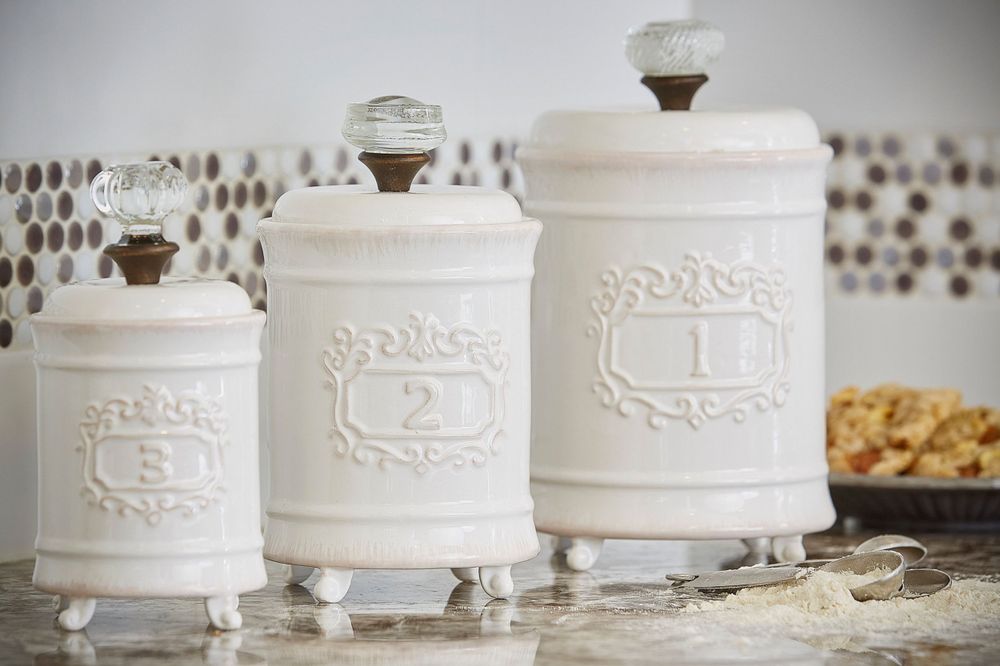 Three sizes of ceramic kitchen canisters, numbered 1, 2, & 3, sit on a counter surrounded by baking supplies and cookies