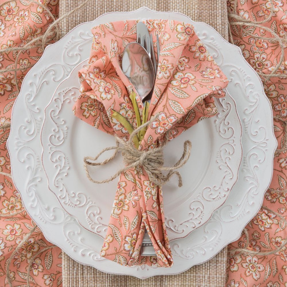 A table setting seen from above. Silverware bundled in a floral pattern napkin sitting on a stack of decorative plates.
