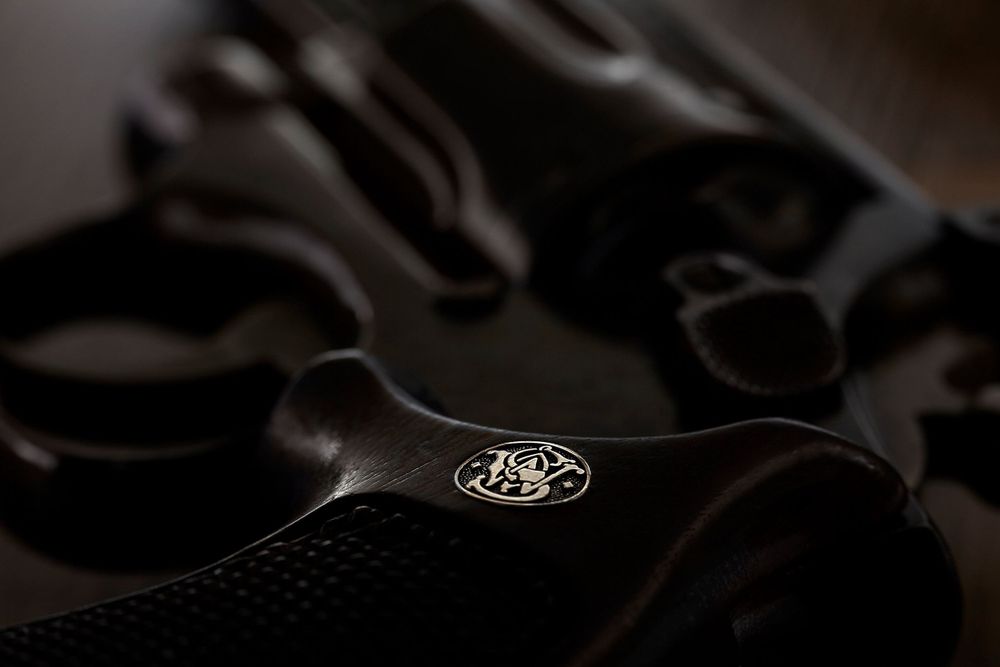 Using low-key lighting, a Smith & Wesson revolver is laid on a dark table with the focus on the gold S&W logo.