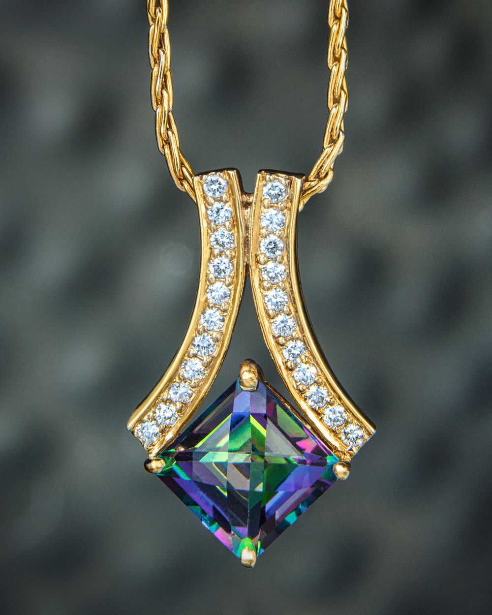A square cut alexandrite gemstone is set in a custom yellow gold and diamond pendant that is hanging on a gold necklace.