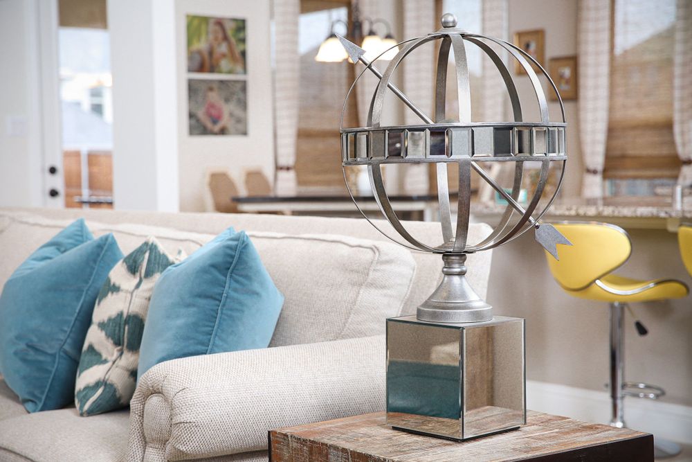 An abstract globe piece of decor sitting on a table next to a couch covered with blue and white throw pillows.