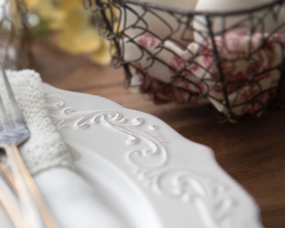 A detail photograph of an ornately scrolled plate rim with a folded napkin and a gold trimmed fork.