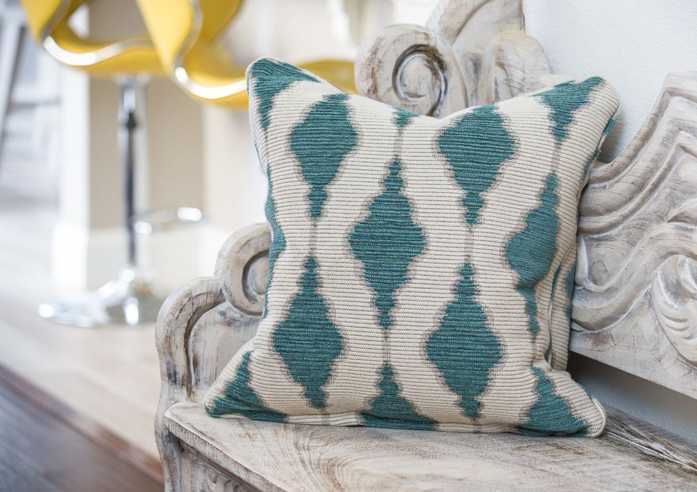 A teal and while colored, diamond patterned throw pillow sits on a white washed hallway bench.