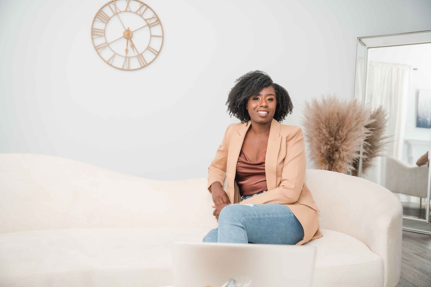 Casual portrait on white couch with decorative clock and pampas grass in background.