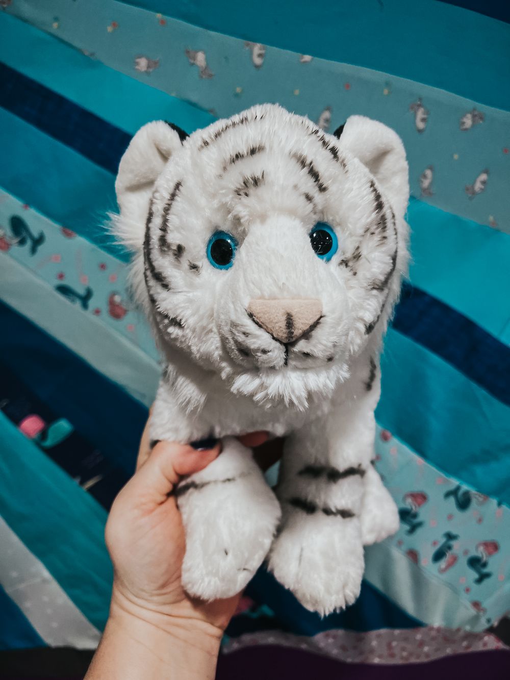 A white stuffed tiger held up with a blue quilt in the background.