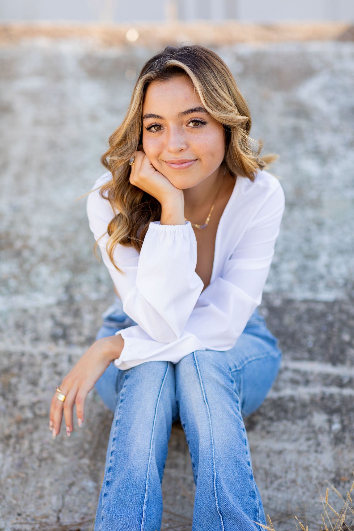 Casual portrait of a high school senior in white shirt and jeans sitting on concrete steps outdoors.