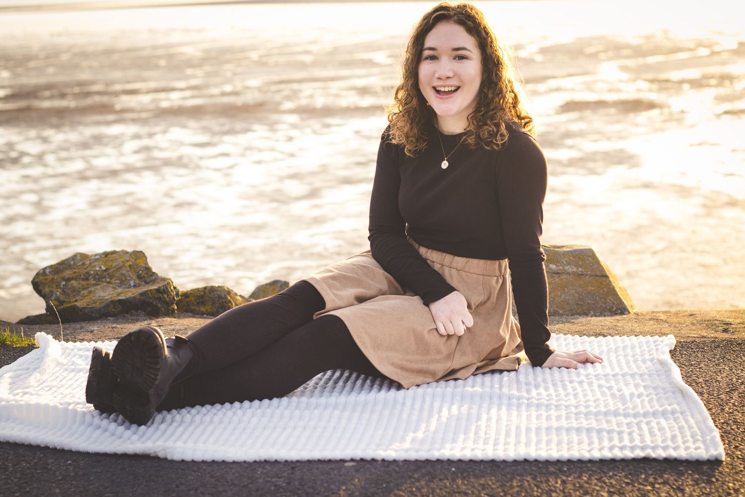 A relaxed sunrise beach portrait on a striped blanket with rocks and golden light in the background.