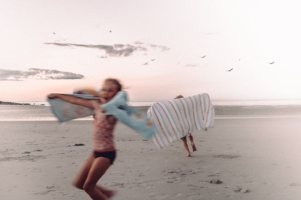 Blurred motion shot of person running on beach with flowing fabric at sunset.
