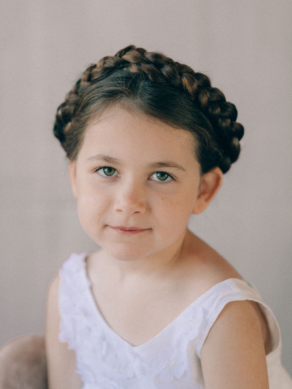 Close-up portrait of child with intricate crown braid hairstyle wearing white top.