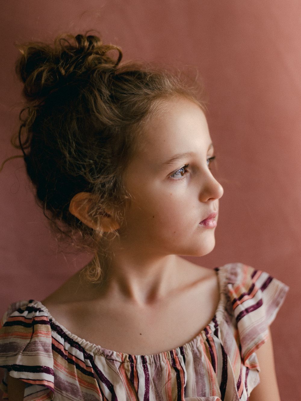 Side profile portrait against warm terracotta background wearing ruffled dress.