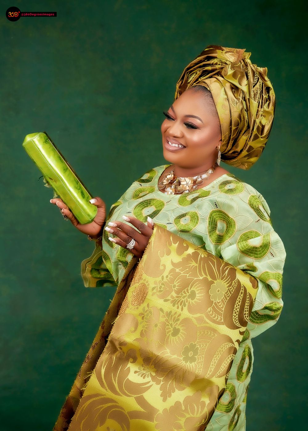 Smiling woman in green gold Nigerian traditional dress holding green clutch purse with matching gele headwrap.