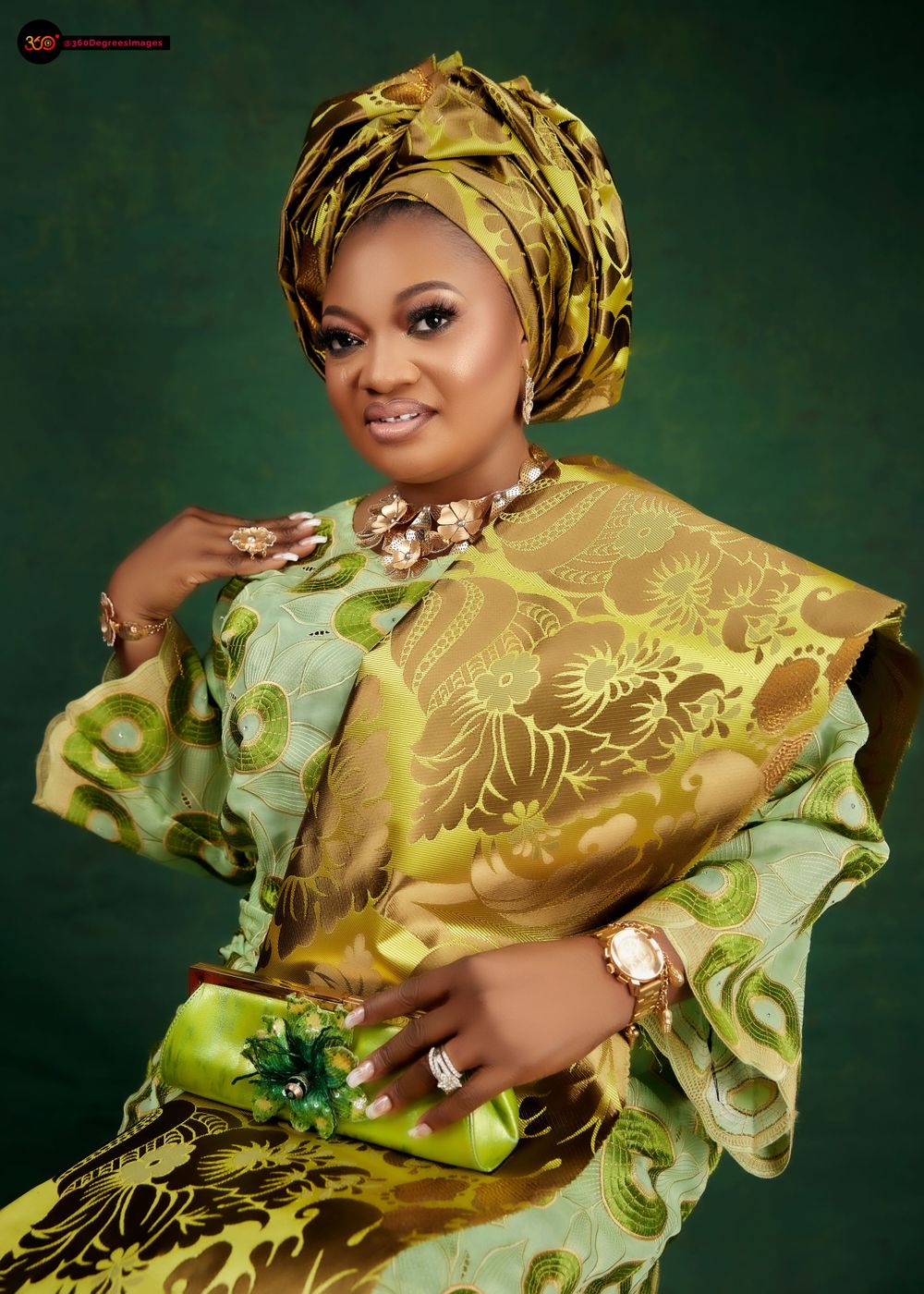 Woman in green and gold African attire with matching gele headwrap and floral necklace poses elegantly.