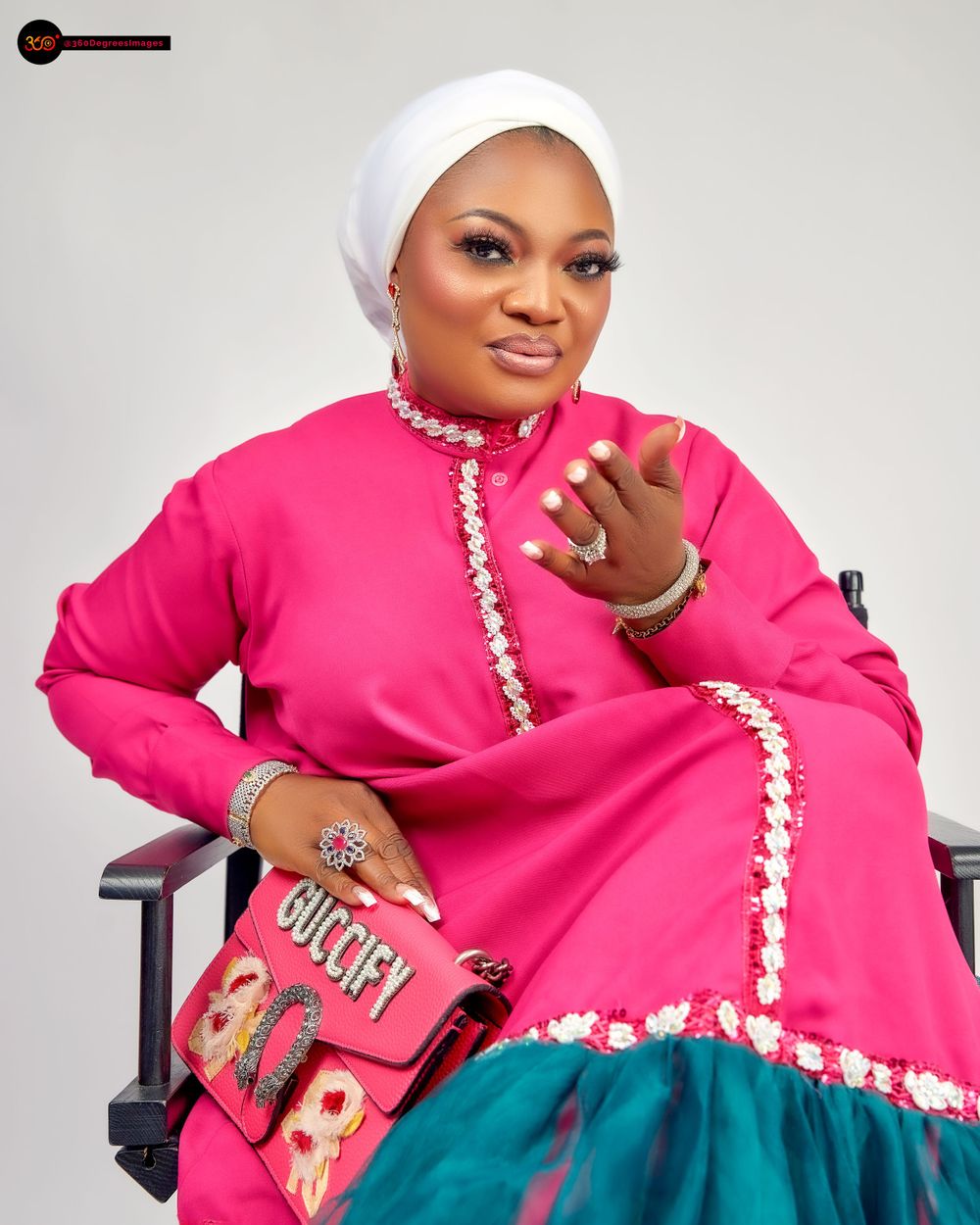 Nigerian woman in hot pink traditional outfit with white hijab holding a Gucci bag in a studio portrait.
