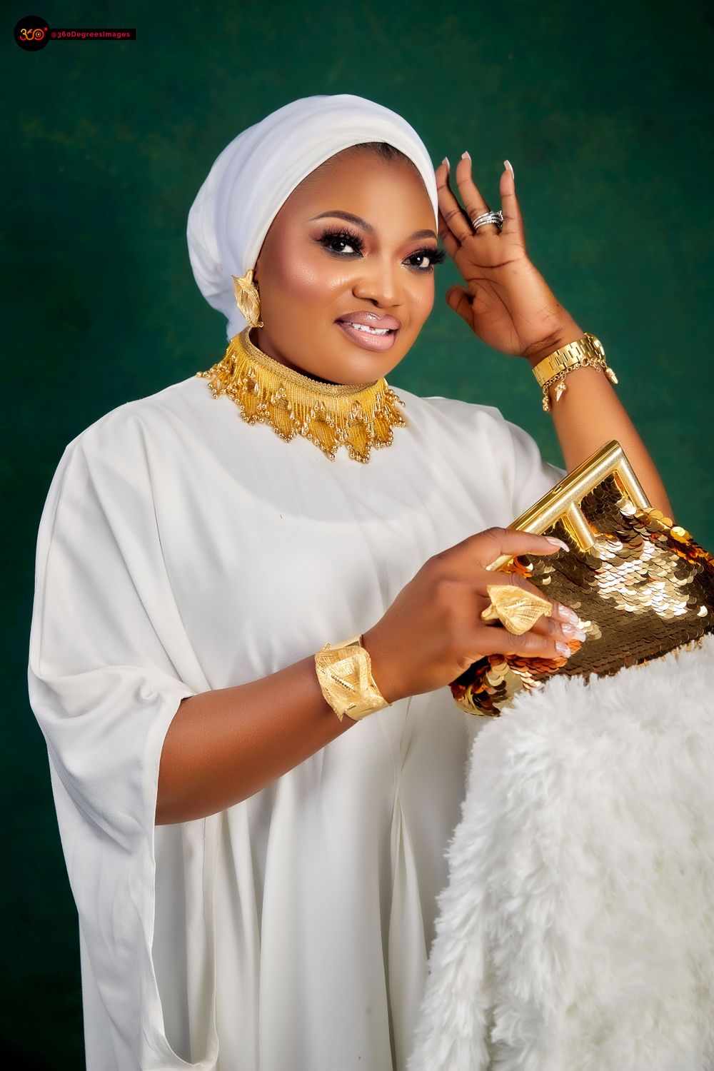 Woman in white Islamic dress with gold jewelry, necklace, bracelets, and sequin clutch poses gracefully.