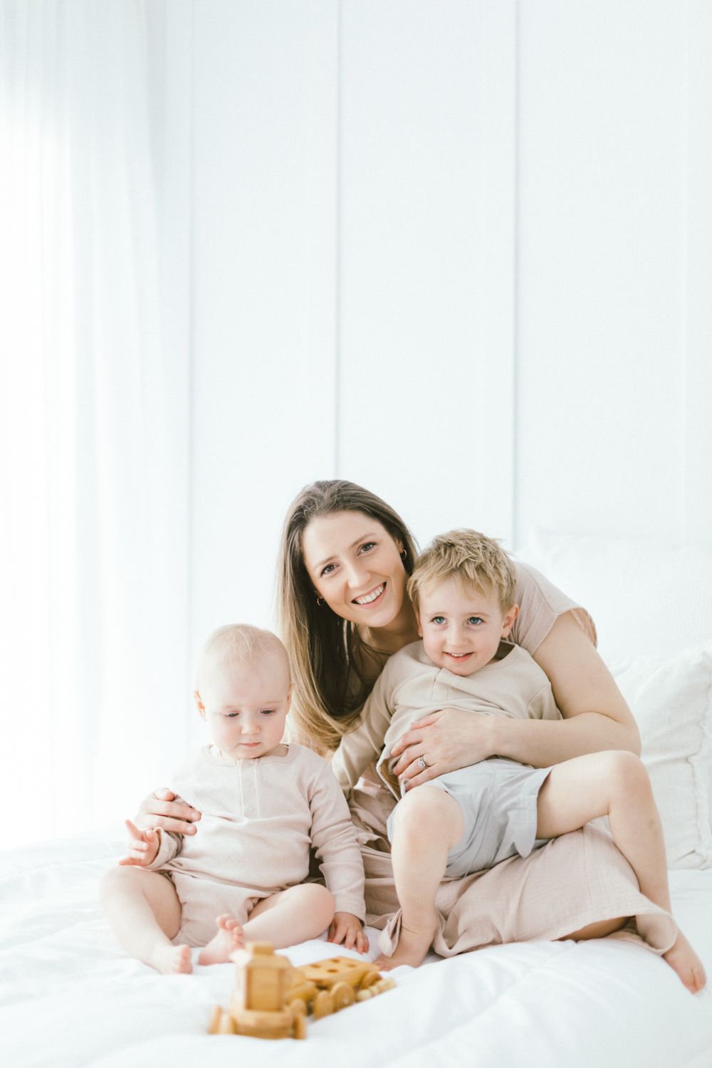 Intimate family moment captured on white bedding with natural lighting.