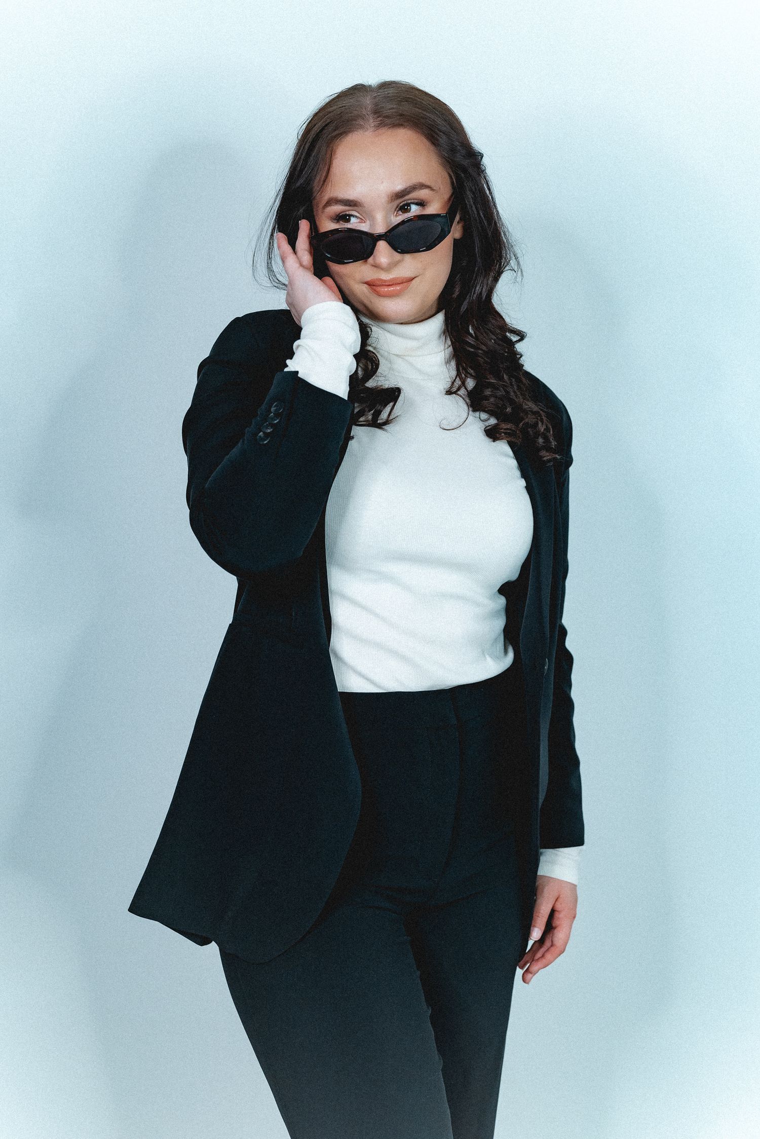 Stylish fashion portrait featuring black blazer, white turtleneck and trendy sunglasses.
