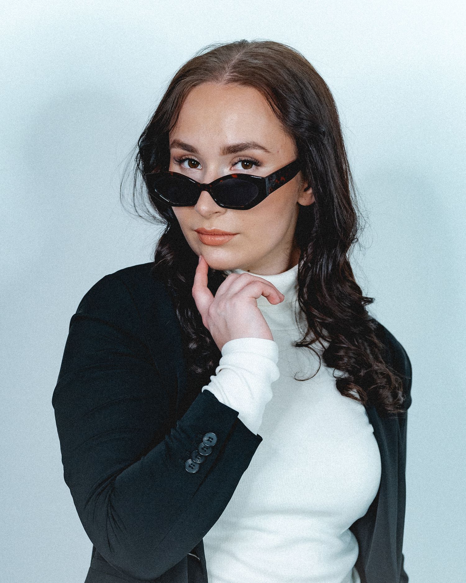 Modern fashion portrait with black sunglasses and white turtleneck against light backdrop.