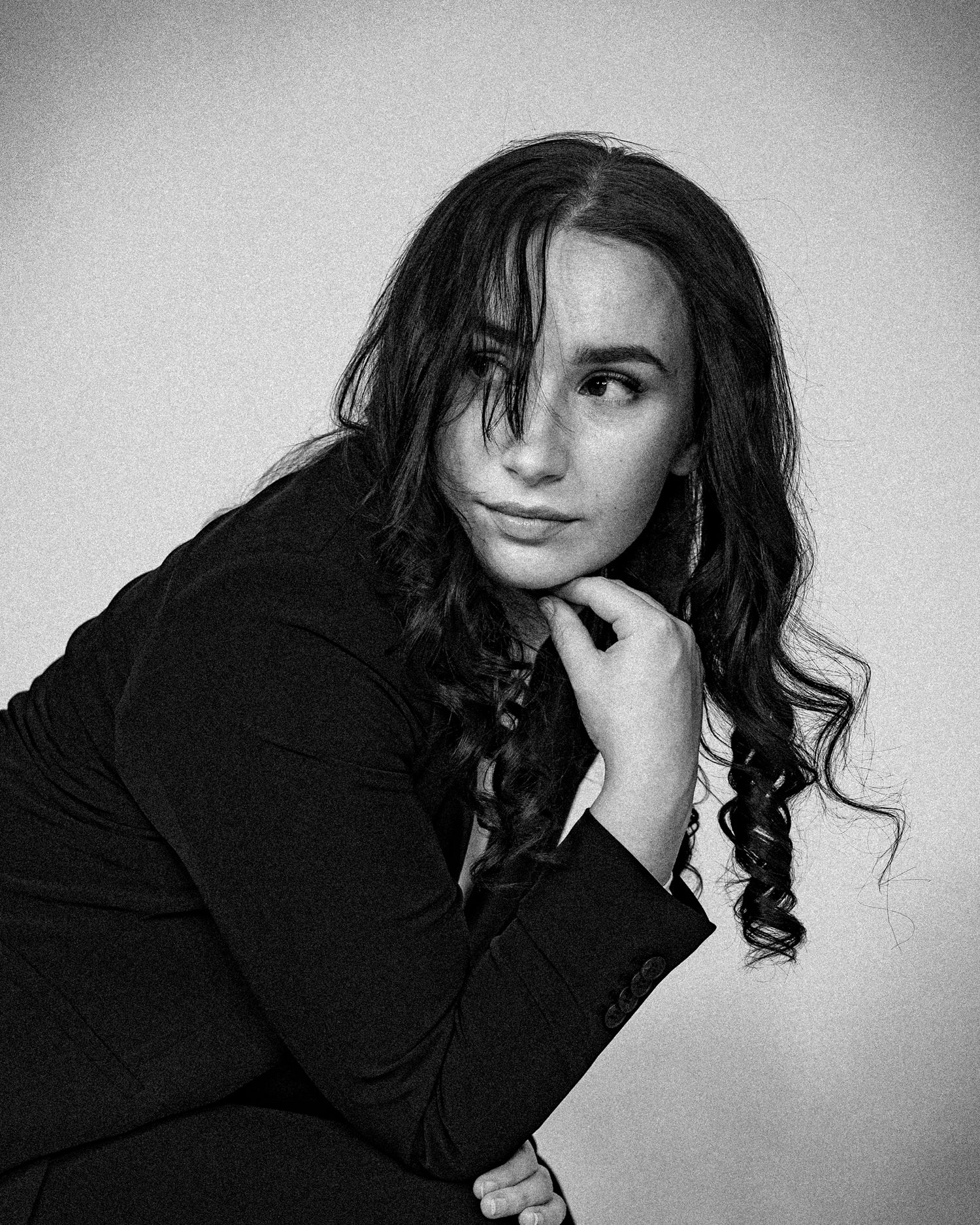 Monochrome portrait with dark blazer and flowing curls against light backdrop.