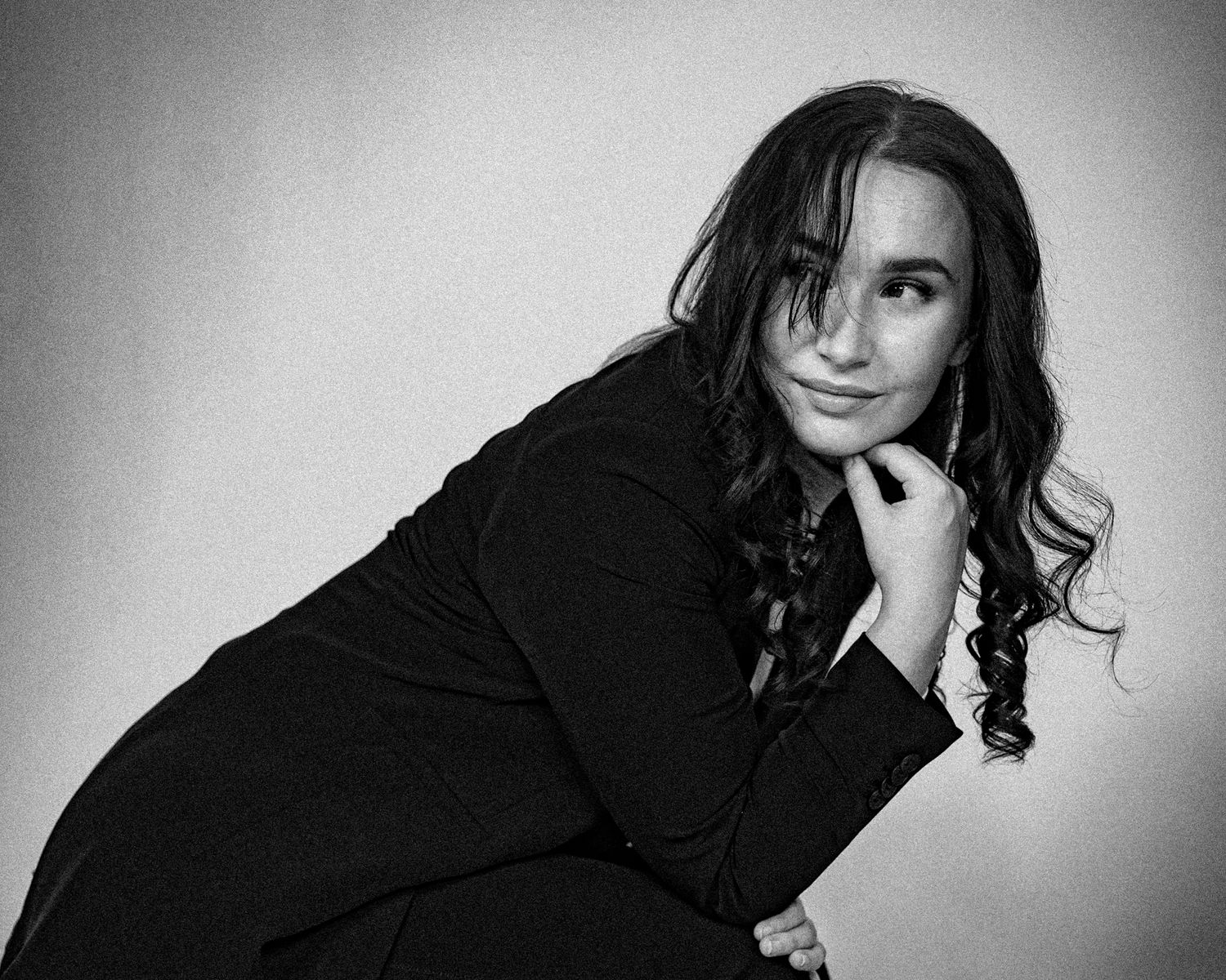 Dramatic black and white fashion portrait with dark clothing and curled hair.