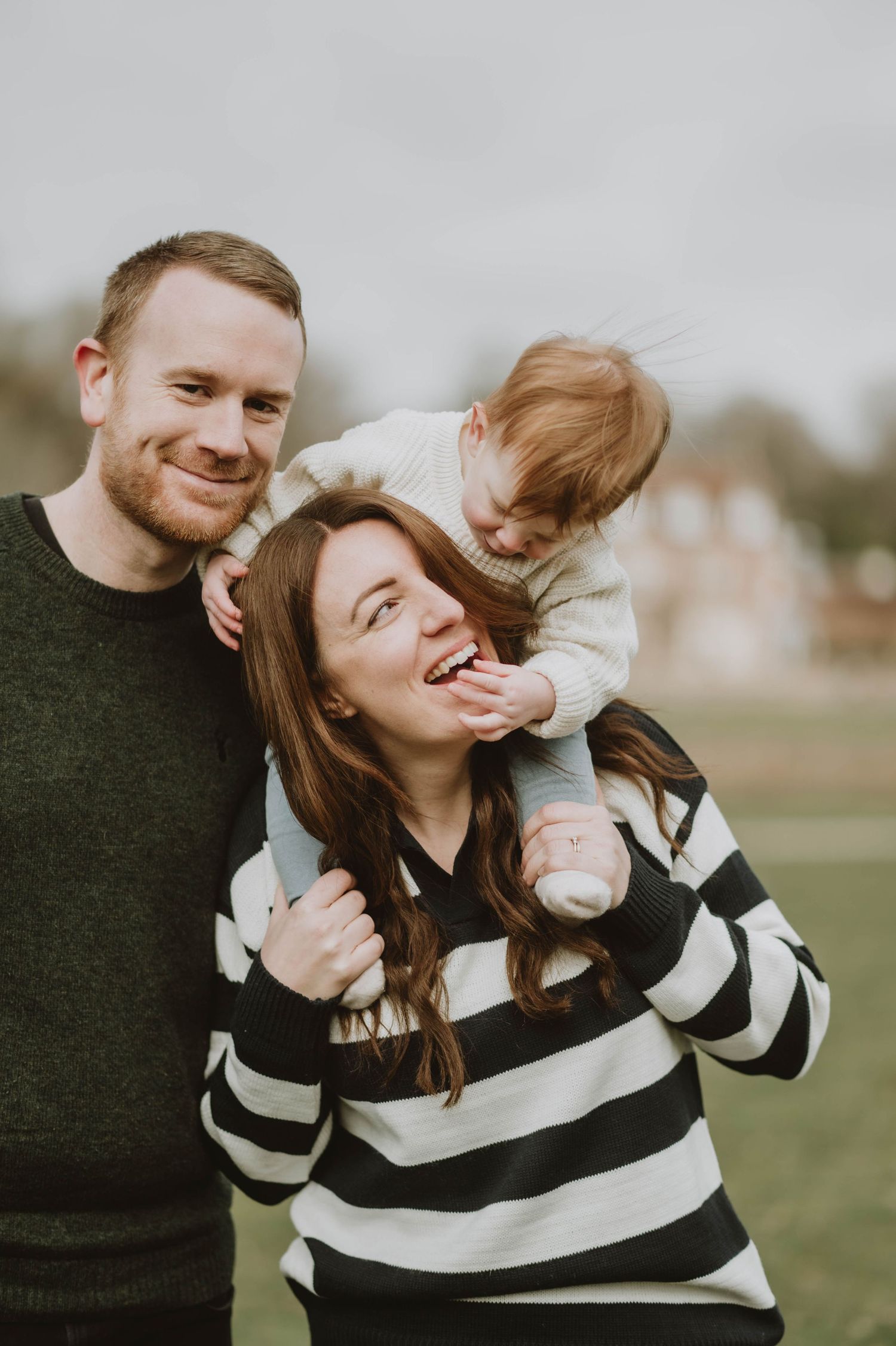 A joyful family moment as a child plays with parents outdoors wearing matching sweaters.