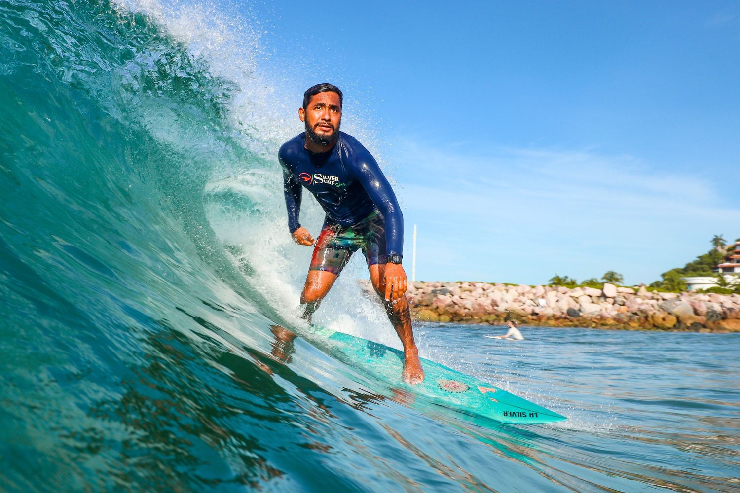 Ixtapa surf photography of a male surfer riding a turquoise wave near a rocky jetty.