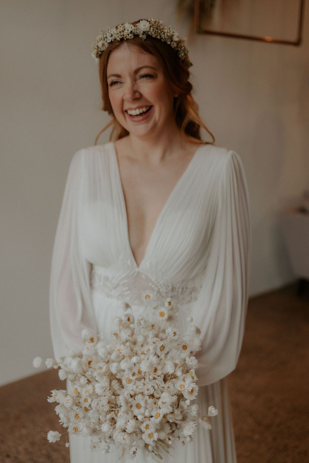 Elegant bridal portrait featuring a pleated v-neck gown and dried flower bouquet in warm tones.