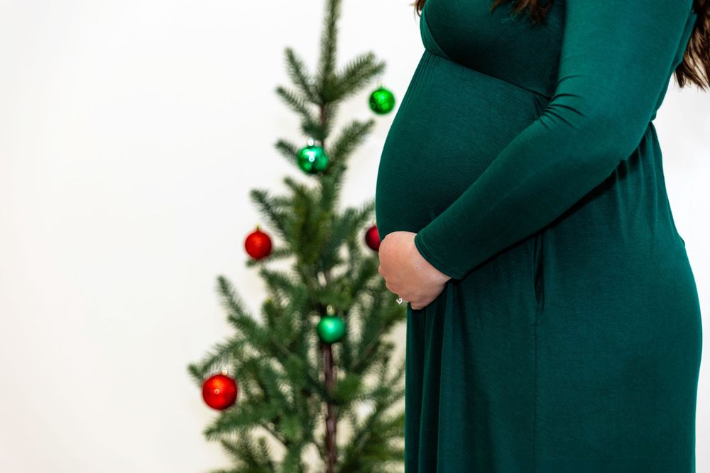 A maternity photo, the woman is in a green dress in a Christmas setting.