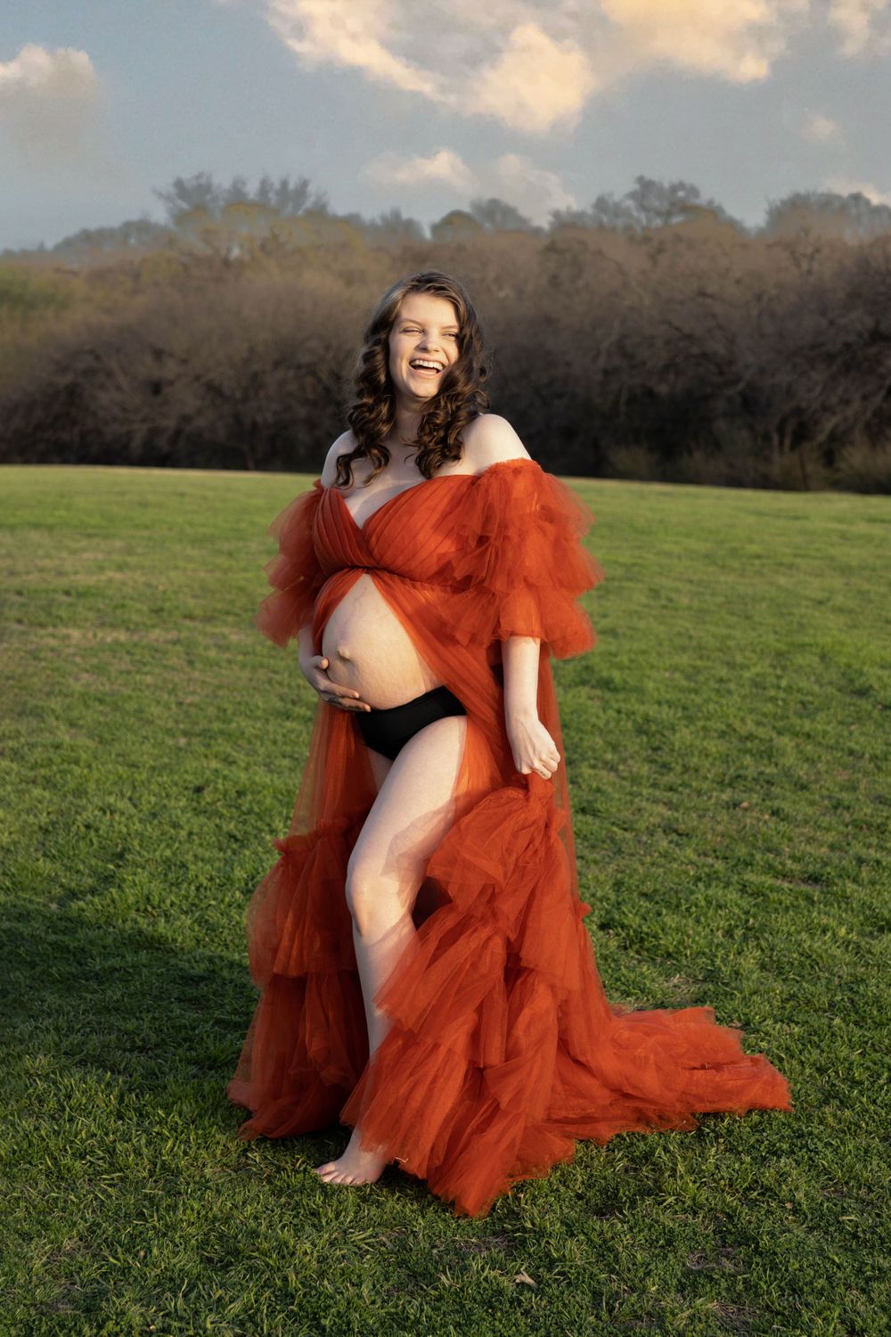 A maternity photo of a woman in a beautiful open front orange maternity gown.
