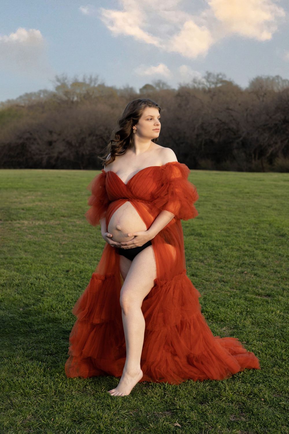 A maternity photo of a woman in a beautiful open front orange maternity gown.