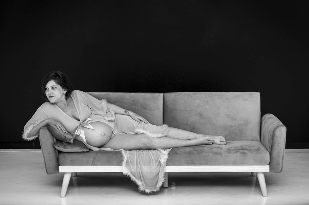 Black and white image of a pregnant woman posing on a couch.