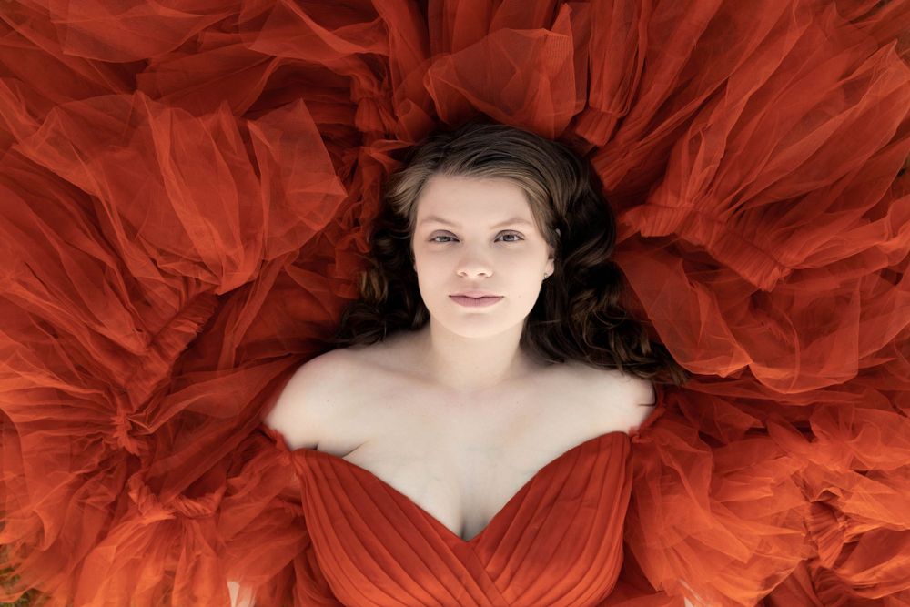 A woman poses laying down surrounded by a beautiful orange dress.