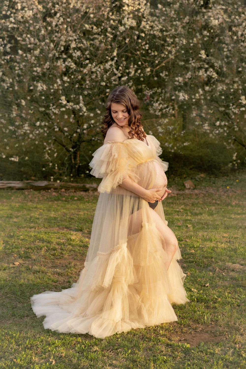 A maternity photo of a woman in a beautiful open front yellow maternity gown.