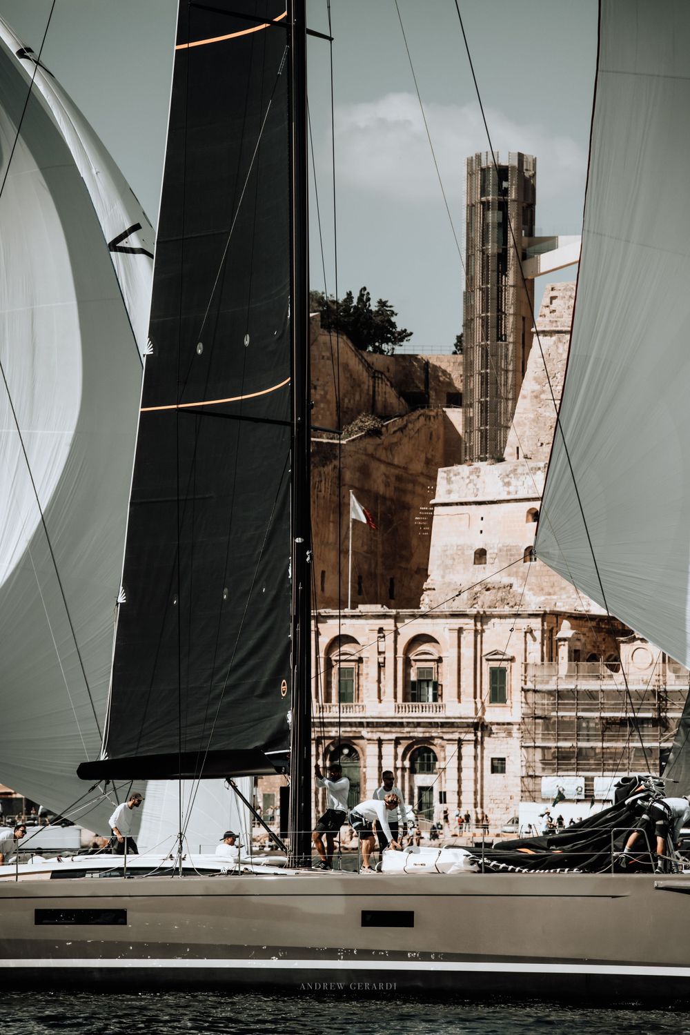 White sails frame historic Mediterranean architecture during a sailing competition.