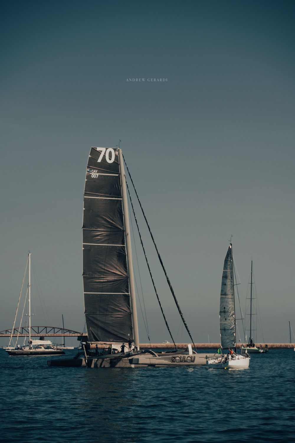 Racing sailboats with dark sails competing on deep blue waters.