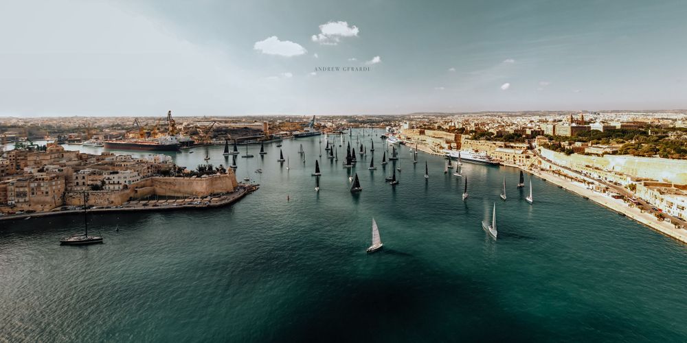 Scenic coastal landscape with multiple sailboats dotting the Mediterranean waters.