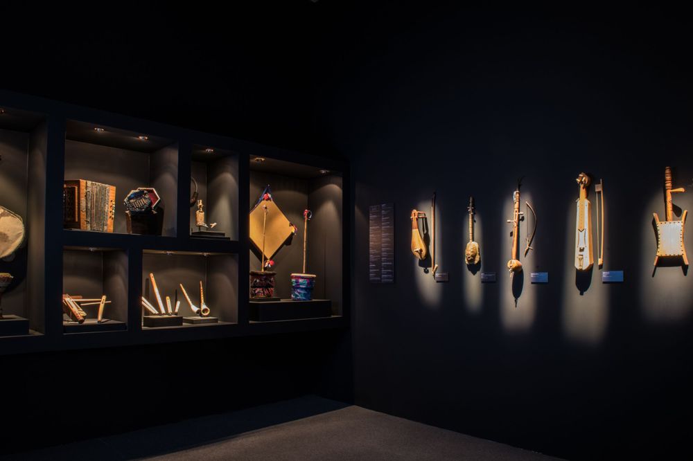 Dark museum gallery with illuminated display cases showing artifacts along the walls.